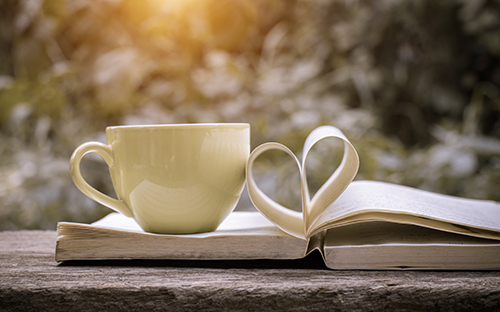 A cup of tea or coffee on top of a book with the pages folded into a heart